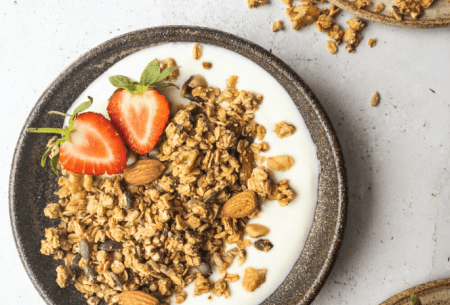 Bowl of yogurt with granola and one fresh strawberry halved