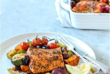 Dinner plate with Wild Alaska salmon fillet on top of traybake mixed roast vegetables, with larger tray of veg in background