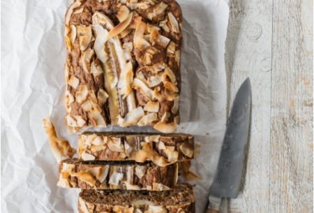 View Banana, fig & courgette loaf One full banana, fig & courgette loaf on bench top, with half cut into individual serving slices