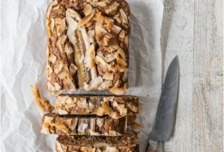 One full banana, fig & courgette loaf on bench top, with half cut into individual serving slices