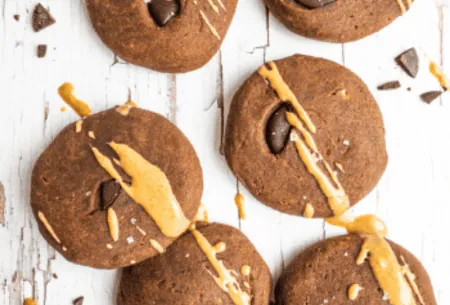 Six chocolate & peanut butter teff cookies on bench top with chocolate chunks and peanut butter drizzle