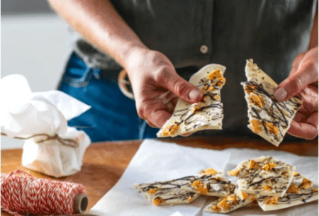 One large piece of prebiotic chocolate bark being broken in half, topped with mango, pistachios and dark chocolate