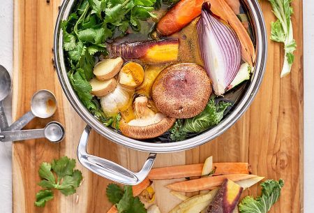 View Busting the bone broth myth A wooden board with a pot of vegetables and broth and herbs inside