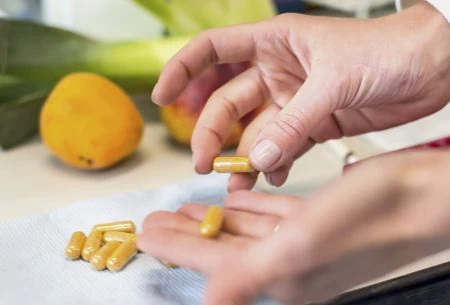 Two hands holding pill capsules over a chopping board