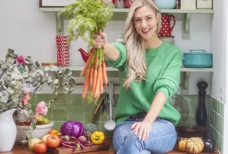 Megan Rossi sat on kitchen surface holding a bunch of carrots