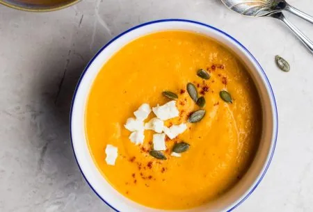 2 bowls of orange soup topped with feta and pumpkin seeds