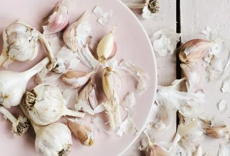 Garlic cloves and bulbs on plate and white wooden surface