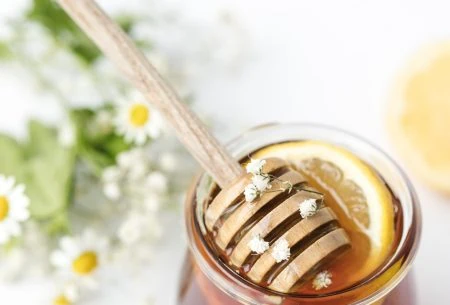 A glass of honey and lemon with a honey spoon in the glass