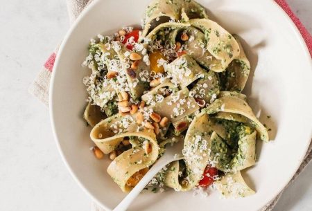 Thick ribbons of pasta and pesto in a white bowl on a red and white cloth
