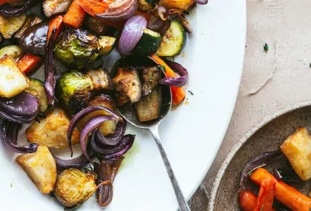 Large serving plate of perfect roast potatoes and mixed vegetables being served onto dinner plate