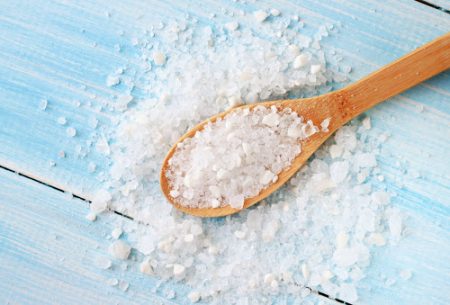 Salt on a spoon and surrounding the spoon on a blue wooden surface