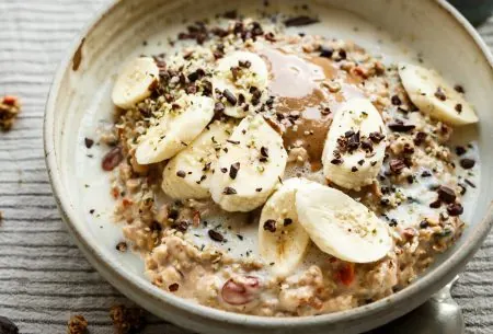 Bowl of porridge topped with banana, grated chocolate and hemp seeds