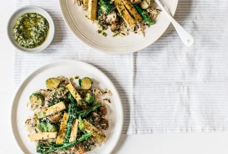 Two plates with Brussels sprouts & tenderstem broccoli & wild rice, served with a small pot of pesto between them