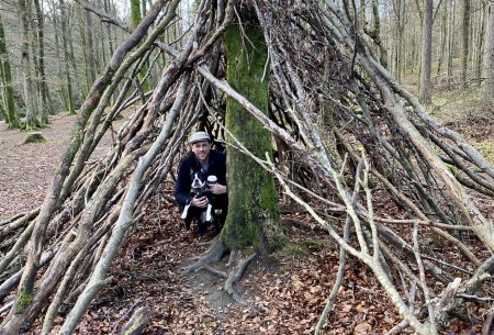 A cave in the woods made of sticks with man and dog inside