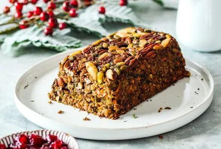One entire baked festive nut roast, with end piece sliced off to show inside. Served with small pot of cranberry sauce