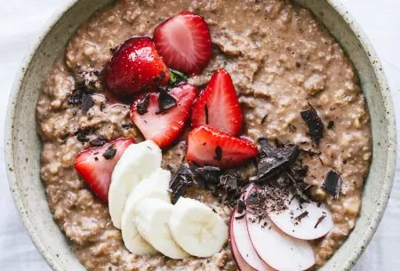 One large bowl full of creamy chocolate porridge, topped with mixed fresh fruit and small chocolate chunk pieces