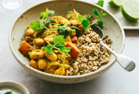 One bowl of cooked sweet potato and butter bean curry, with portion showing half grains and half curry. Served with a spoon