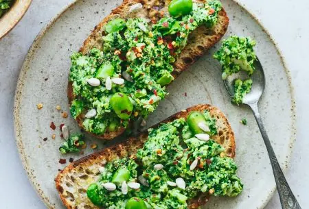 Two pieces of toast on a plate, spread thick with broad bean chilli paste and mixed seeds