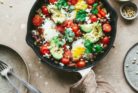 Cast iron skillet sitting on bench top with fresh cooked mixed bean shakshuka, garnished with fresh coriander