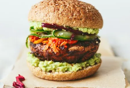 One stacked spicy miso mushroom burger with all ingredients layered between a burger bun, displayed on a chopping board