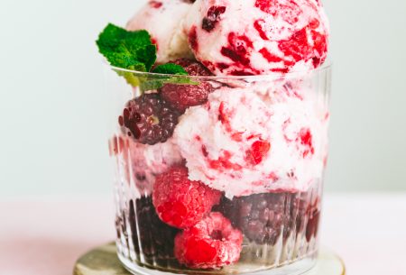 One glass jar overflowing with two large scoops of kefir ice cream. Garnished with frozen berries and fresh mint leaves