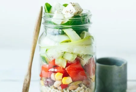 One large zingy salad jar displayed in a mason jar and layered with salad ingredients. Small pot of dressing on the side