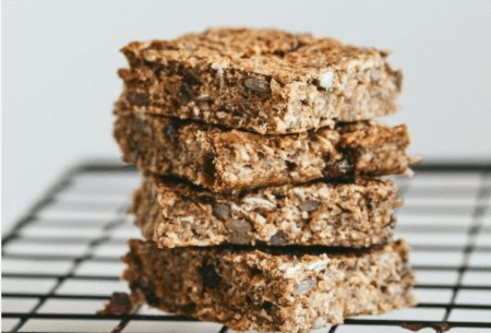 Four nutty banana fibre-filled flapjacks stacked on a wire cooling rack