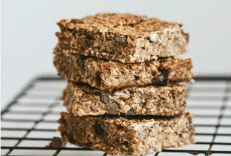 Four nutty banana fibre-filled flapjacks stacked on a wire cooling rack