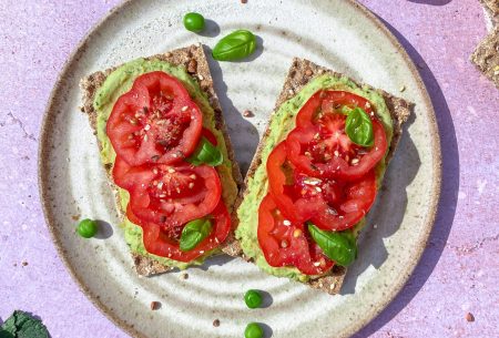 Two pea and mint hummus crackers with fresh tomato slices, displayed on a white plate with a purple background