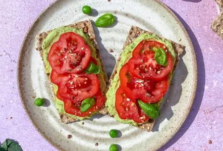 Two pea and mint hummus crackers with fresh tomato slices, displayed on a white plate with a purple background