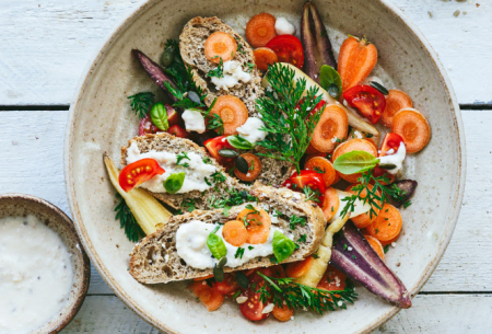 Ceramic bowl with quick carrot caesar salad, served with fresh brown bread slices and garnished with fresh mixed green herbs