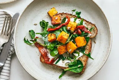 One piece of bread shown as an open sandwich with butternut squash, feta and fresh greens