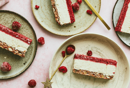 Three slices of raspberry and cashew cheesecake on light green plates, with fresh raspberries scattered