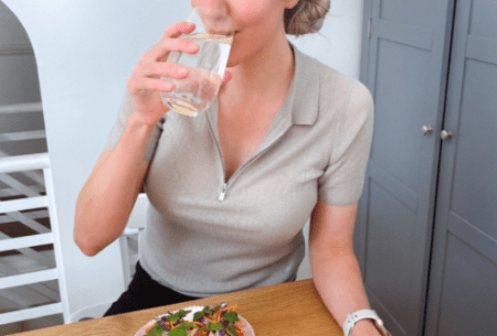 View Drinking water with meals: yay or nay? Dr Megan Rossi sitting at a table drinking a glass of water with a small plate of snacks in front of her