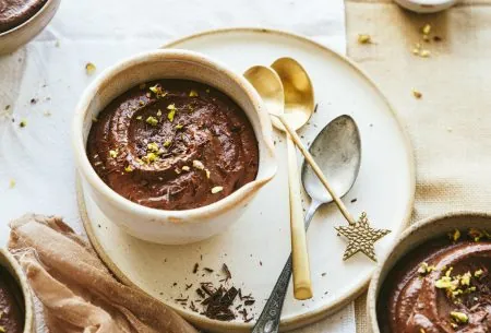 One pistachio and chocolate pot served in a bowl. topped with pistachios and displayed on an additional plate