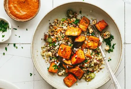 Roast aubergine with mixed grains and red pepper sauce, on a white place with a pot of extra sauce