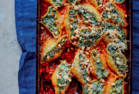Oven tray full of freshly baked spinach and ricotta pasta shells with serving spoon
