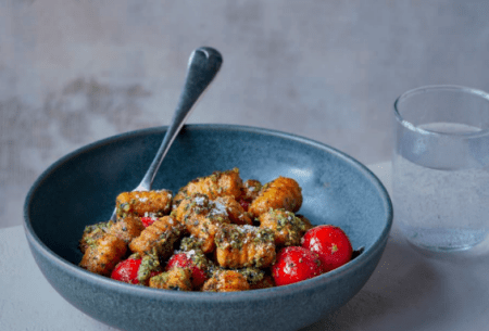 A blue bowl of sweet potato gnocchi covered in super pesto