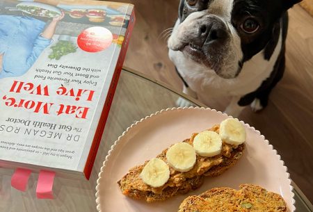Two pieces of bread topped with banana slices, showing dog and The Gut Health Dr book 'Eat Well, Live More' in background