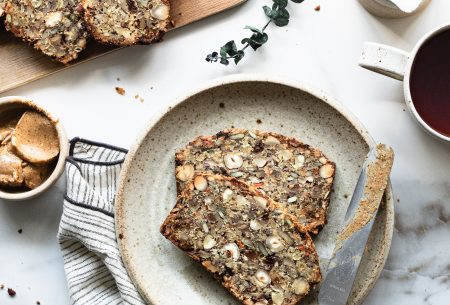 Two pieces of Nordic style super seedy and nutty loaf with figs, with knife and nut butter spread