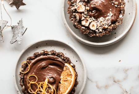Two chocolate granola tarts on plates, decorated with fresh fruit and nuts