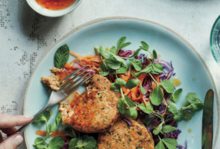 Two cooked fishcakes on top of a fresh, crunchy salad with a pot of homemade dressing