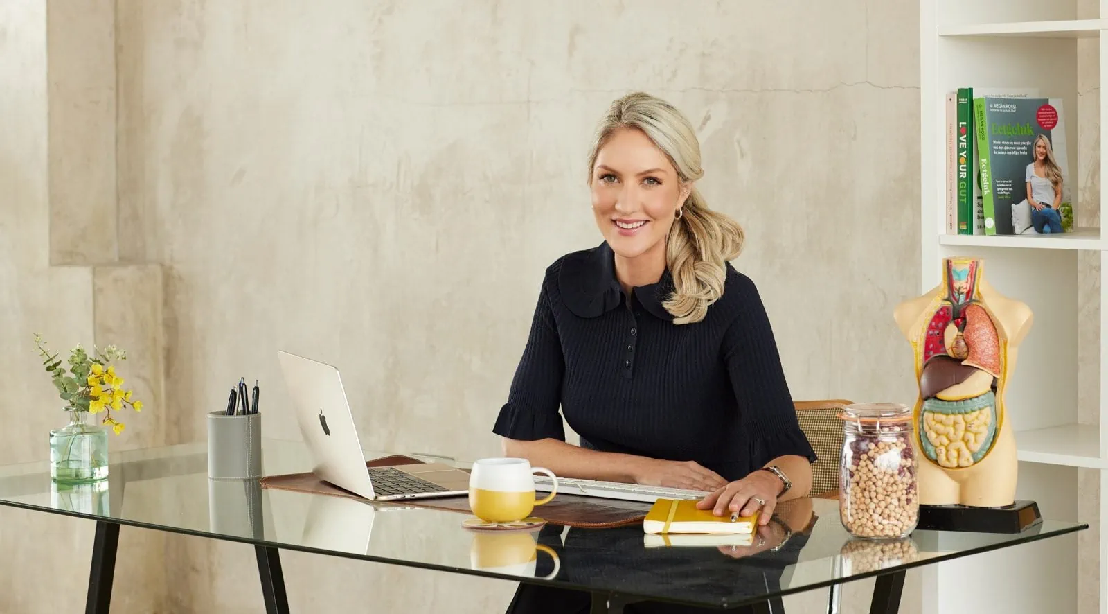  Photo of Dr Megan Rossi, founder of The Gut Health Doctor, seated at a desk looking professional and smiling at the camera