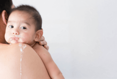 Small baby being held on the shoulder of a woman to show the baby's face and some drool running down the women's back