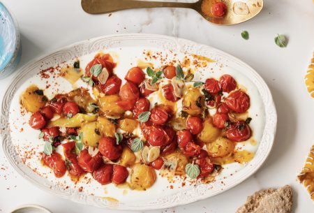 Red and orange cooked tomatoes displayed over cold yogurt on a long, ceramic plate
