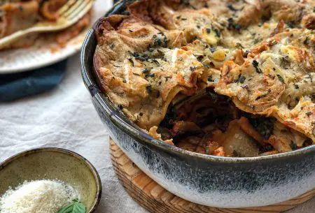 Large serving dish on bench filled with fresh cooked lasagne, one piece cut away to show inside