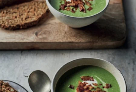 Fresh baked brown wheaten bread displayed on a chopping board with a bowl of soup