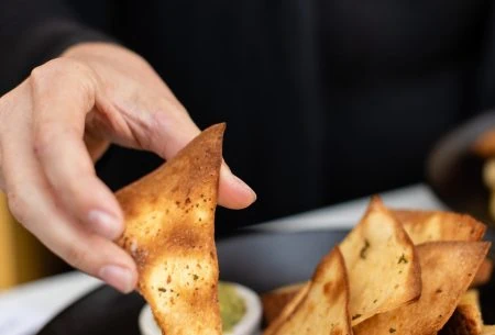 A hand holding crackers with various dips available for snacking