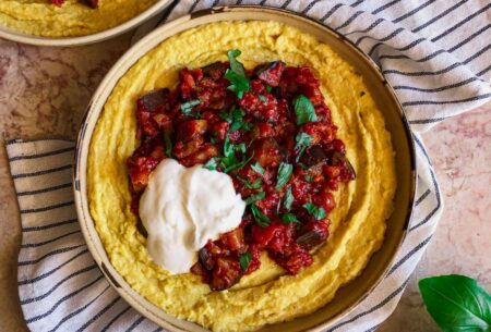 Bowl of sweetcorn polenta topped with aubergine ragu, chopped basil and a dollop of yogurt