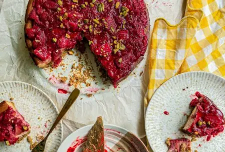 Photo of strawberry and pistachio cheesecake and two plates with slices of cheesecake that are half eaten